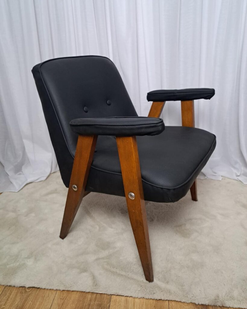 Retro fotel klubowy typu „Lisek” z okresu PRL, tapicerowany czarną eko-skórą, na charakterystycznych drewnianych nogach.